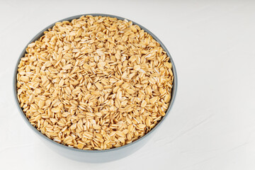 Oat flakes bowl on a white background. Raw oatmeal for a healthy breakfast. Copy space. Top view