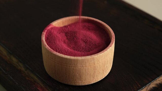 Beetroot powder is poured into wooden bowl, close-up. Selective focus. Food additive E162, natural pigment beet red. Dry beet powder. Superfood, antioxidant.