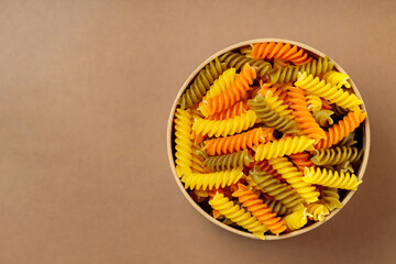 Tricolor fusilli pasta in a cardboard box. Raw fusilli pasta on a beige background. Copy space