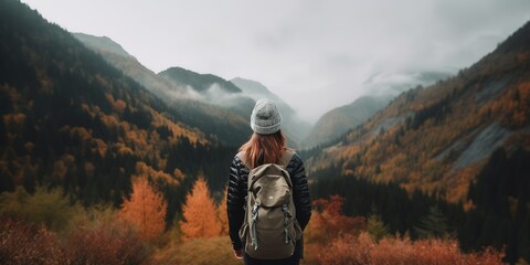 A woman with a backpack stands in a mountain landscape. - obrazy, fototapety, plakaty