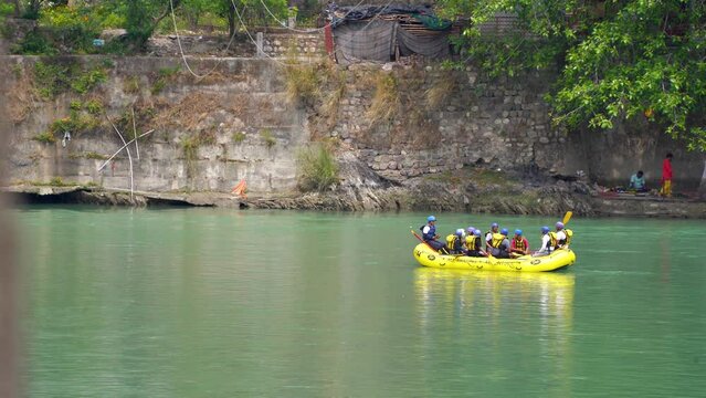 wide shot of yellow raft with people enjoying adventure sports floating on the green waters of the ganga in rishikesh haridwar for this popular summer adventure sport