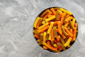 Fusilli pasta with spinach and tomato on a gray background. Raw colorful italian fusilli pasta in a...