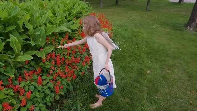 Cute angel girl with wings on her back. In her hands is a bucket of paint she paints.