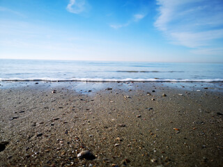 Sand beach low angle closeup with smooth water. Small waves rolling on the beach. Clear blue sky on a sunny summer day. 