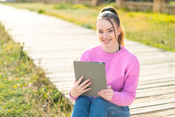 Young pretty girl holding a tablet at outdoors smiling a lot