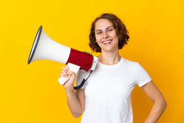 Young English woman isolated on yellow background holding a megaphone and smiling