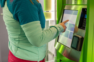 A young woman buys a public transport ticket in a vending machine, urban and agglomeration transport - obrazy, fototapety, plakaty