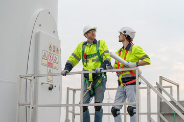 Two engineer in uniform with helmet safety pointing and holding blueprints to inspection and maintenance of wind turbine in wind farms to generate electrical energy, Renewable power energy.