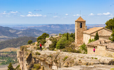 Fototapeta na wymiar People on the cliff enjoying the view over the mountains and the church in Siurana, Spain