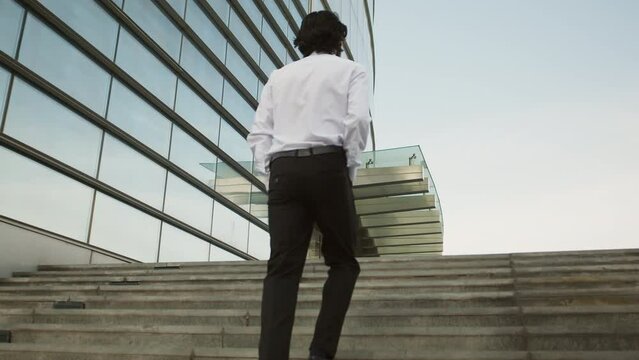 Young asian businessman in a white shirt in a rear view climbs up the stairs to the entrance of the business center to continue solving corporate issues