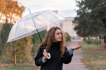 Girl with an umbrella on cloudy autumn day. Portrait of young woman with long brown hair standing outside with umbrella.