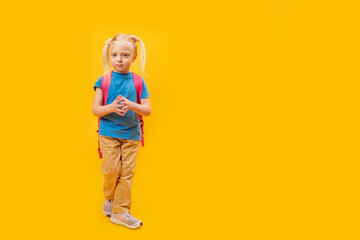 Full-length portrait of little girl with backpack on bright yellow background. Primary school...