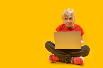 Schoolboy sits with laptop in his hands and looks carefully at the monitor. Modern education. Programming for children.