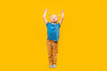 Full-length portrait of little girl with two ponytails, looking up. Happy preschooler in blue T-shirt on yellow background