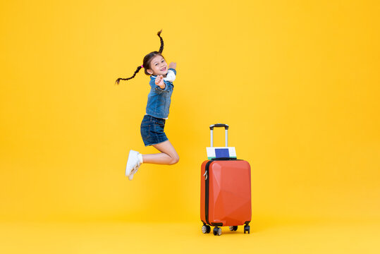 Jumping excited cute little girl with luggage in isolated yellow color background studio shot, minor travel concept