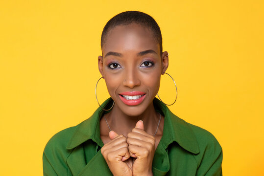Headshot portrait of fashionable skinhead African American woman face with big earrings against yellow color background studio shot