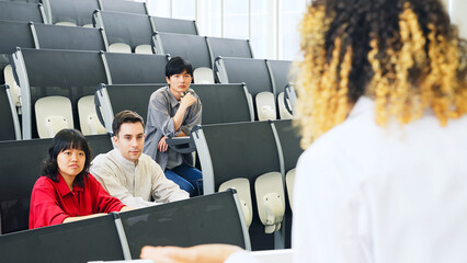 A female lecturer giving a lecture in the auditorium and multinational students listening.