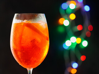 Glass of Aperol Spritz cocktail on a blurred background with colorful bokeh. Aperol spritz cocktail, close up. Alcoholic cocktail concept at a party. Copy space
