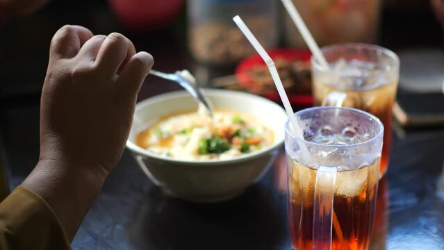 Person eating chicken porridge on the table. Eting bubur ayam.