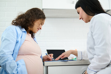 Confident pregnant woman signing declaration with a family doctor, concluding a contract about...