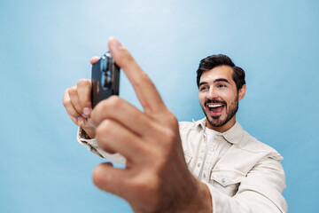 Portrait of a stylish man brunette smile and open mouth looks at the phone blogger with a beard, on a blue background in a white T-shirt and jeans, copy space