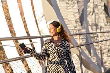 smiling latina woman listening to music with a headset on a sunny day in the city