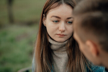 Sad young woman looks at a man in the park, quarrel, question
