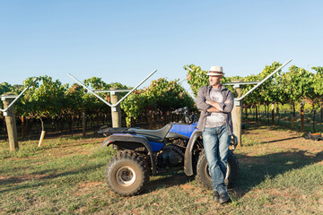 Winemaker in straw hat standing near quad bike