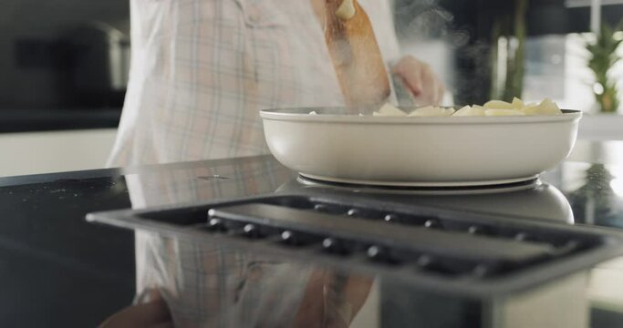 Adult woman fries potatoes on an induction electric stove with a built-in extractor fan