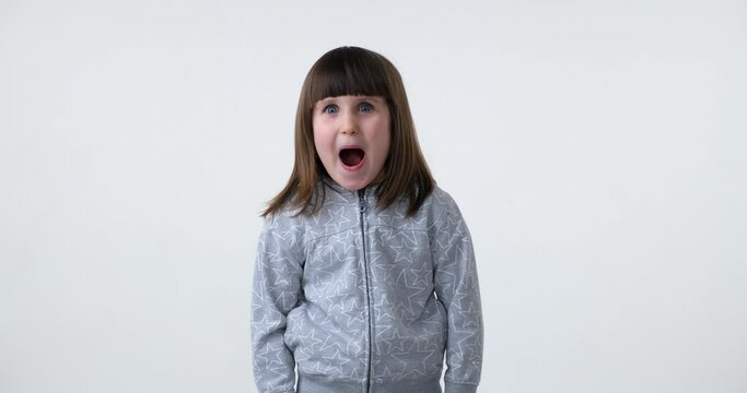 Adorable preschool girl standing on white background looks into the camera with a big smile, then sees something incredible and exclaims Wow in amazement.