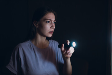 Woman scared holding hand flashlight in darkness and afraid of violence criminal robbery - obrazy, fototapety, plakaty