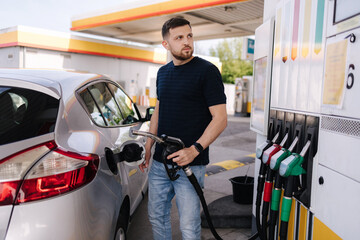 Handsome bearded man refueling car and looking on the scoreboard while standing on self service gas...