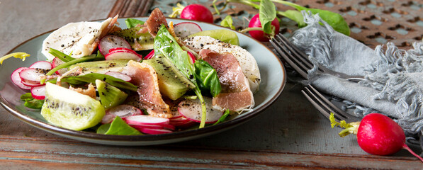plate with salad with radish and kiwi on a wooden table