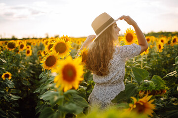 Happy young woman surrounded by yellow sunflowers in full bloom, in a flower garden, traveling on...
