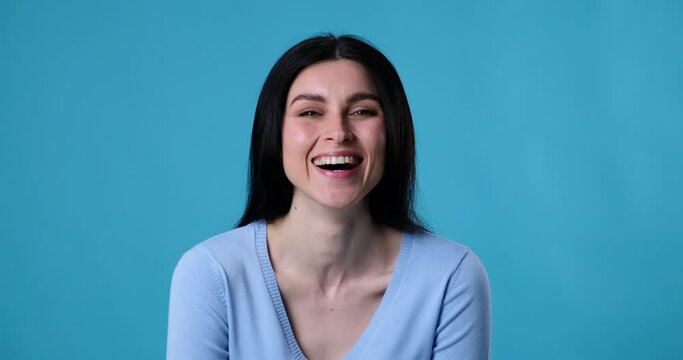 Caucasian woman stands on a blue background, laughing loudly and smiling at the camera. She poses with her arms crossed and exudes joy, friendliness, and satisfaction.