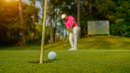 Golfer putting ball on the green golf, lens flare on sun set evening time.