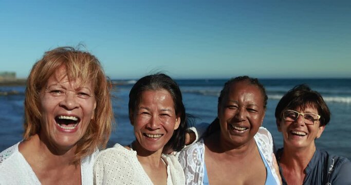 Happy multiracial senior women having fun together smiling in front of camera on the beach wearing summer clothes - Joyful elderly lifestyle, vacation and travel concept