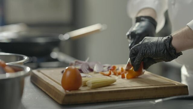 Male chef cuts salad ingredients in restaurant on wooden board. Slicing vegetables close-up. Slow motion