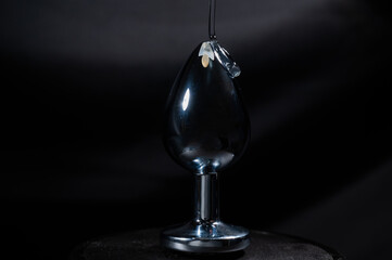 Intimate lubricant is poured onto a steel anal plug on a black background. 