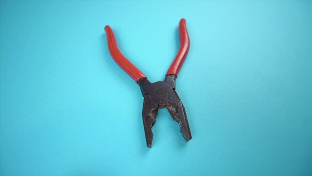 old pliers with red plastic handles on light blue background