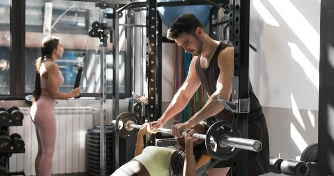 Man helping a woman doing bench press in a gym