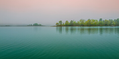 Obraz premium Trees, water reflections, and the pink sky. Tranquil Maine coastal road seascape over Casco Bay on Bailey Island on a foggy morning.