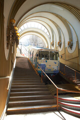 A blue and white cable funicular rises on rails along the slope. Funicular tram, side view. Station...