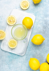 A cup of squeezed lemon juice and lemons, slices of lemons around. Bright background. Summer concept