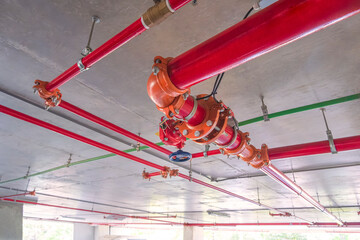 Red fire protective water pipeline system on concrete ceiling inside of parking garage building, selective focus 