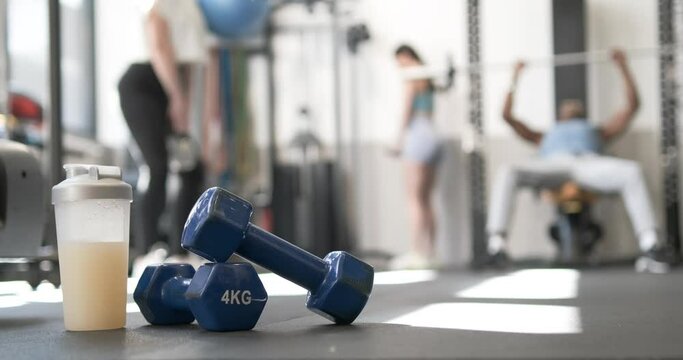 Dumbbells and a supplement shake in a crowded gym