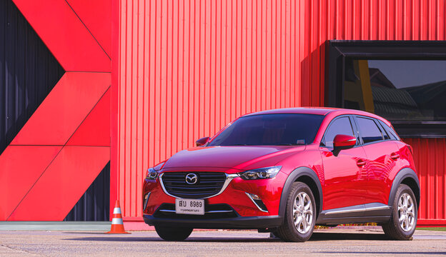 Samut Sakhon, Thailand - May 18, 2023: Red Mazda2 modern car parked in parking lot area in front of red and black metal building wall in industrial style, illustrative editorial
