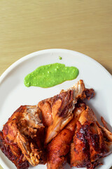 Grilled chicken with green sauce on white plate on wooden table.