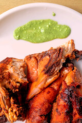 Roasted chicken with green sauce on a white plate close up