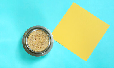 South Indian homemade filter coffee cup and yellow paper on blue background, top view